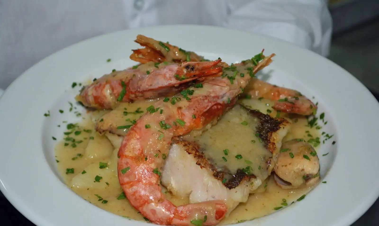 Un plato de merluza con gambón y almeja en salsa, con cebollino picado